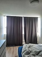 Two dark grey drape panels hanging on curtain rod covering two windows, showing full length and fit.