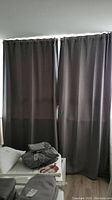 Full view of two grey IKEA drapes hanging on a window with some daylight filtering through.