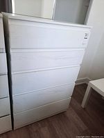 Front view showing the white dresser with five drawers, some minor scratches and flat drawer fronts.