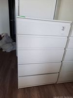 Front view of the white IKEA dresser showing all five drawers closed with minor surface scratches visible.