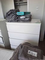 Front view of white dresser with five drawers, folded linens on top.