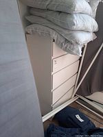 Side angle showing 5-drawer white IKEA dresser covered partially with bedding and beside a mattress and some metal poles.