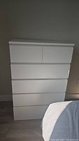 Front view of the white IKEA dresser showing six drawers (two small top drawers, four large lower drawers) with integrated groove handles.