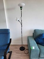 Full view of black IKEA floor lamp showing the two light fixtures, one large top lamp and one smaller adjustable lamp below, and cord running down to weighted base.