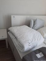 White king size duvet folded on a bed with a side table and pillows in the background