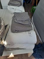Folded king size gray duvet and matching cover placed on white bed frame against mattress and wall, clearly showing knit pattern cover and quilted duvet.