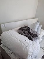 King size white duvet folded on bed with grey blanket and stacked linens including pillowcases.