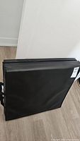 Foldable black mat folded, showing its thickness and carrying handles.