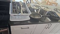 Full set of pots, pans, kettle, utensils, and baking dishes arranged on black countertop with white cabinets.