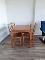 View of the dining table and four chairs from one side showing full set and condition of wood surface and chairs.