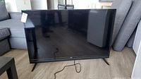 Front view of the RCA 50 inch flat screen TV standing on the floor with two angled legs and power cord attached.