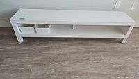 Full front view of the white IKEA TV stand showing two small white storage bins in the open shelf space.
