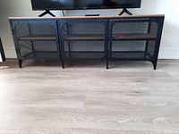 Front view of the IKEA TV stand with a wooden top and black metal frame mesh doors closed.