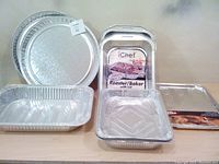 Multiple aluminum trays showcasing round hammered metal trays, rectangular roaster/baker trays with lids and aluminum foil trays.