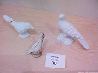 Three white cast iron bird figurines on wooden surface with paint chips and wear visible.