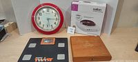 Red and white analog wall clock, Apex Twist digital bathroom scale, wooden cigar box, and boxed Salton single burner cook-top displayed together