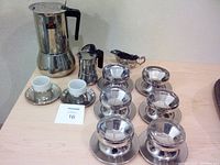 Full lot showing all items together on table: espresso carafe and pot, ceramic cups in holders with saucers, six stainless steel sherbet bowls with saucers, and silver creamer.
