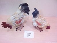 Pair of hand carved wooden chickens, a rooster and hen, side by side on a wooden surface with auction tag number 27