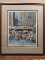 Full view of framed art print showing two dogs near water by cabin with double matting and brown frame.