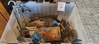 Clear view of painting supplies in plastic bin showing paintbrushes, scrapers, tape, and gloves.
