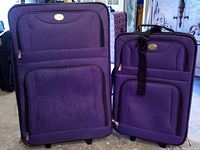 Photo of front view of two purple luggage pieces, one larger and one smaller, showing exterior pockets, wheels, and handles.