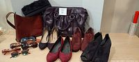 Group shot showing three purses, six pairs of shoes, and six pairs of sunglasses arranged on flat surface