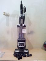 Full view of upright Shark vacuum cleaner with dustbin and attached wand, standing upright with multiple attachments laid out in front.