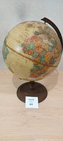 Side angled view of the vintage globe showing the outline of Africa and Europe continents and mounted on a round base with an arm holding the globe.