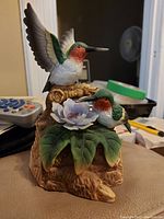 Photo of a small bird statue with two birds on a flower pedestal showing detailed wings, colorful feathers, and a textured base.