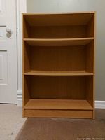 Front view of the light brown particle board book shelf with 2 adjustable shelves visible inside.