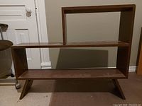 Vintage solid wood bookshelf with a medium brown finish, two shelves of different sizes, and angled legs on carpeted floor against a wall.