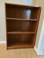 Solid wood book shelf with three shelves and some marks on the surface.