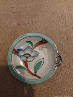 Top view of vintage decorative plate showing the blue flower and colorful leaf design on a pale green rim.