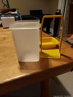 Photo showing Tupperware pickle container and yellow veggie container with draining stand on wooden table.