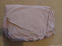 Folded dusty rose colored sheet set including fitted and flat sheets on carpet background.