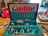 Opened wooden case showing the full silverware serving set for 12 including knives, forks, spoons, carving set, and additional serving utensils arranged inside.