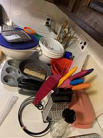 Overview photo showing bakeware including cake and muffin pans, mixing bowls, rolling pin, crocks with kitchen utensils, and colorful cutlery.