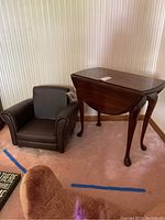 Photo showing the brown leather-like child size chair next to a cherry wood drop leaf end table with Queen Anne legs in corner of a room.