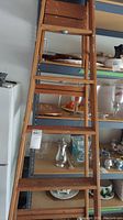 Full height view of the wooden ladder leaning against a shelving unit showing its size and step details.