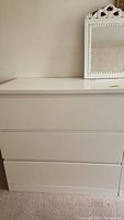 Front and side view of a white laminate three drawer dresser with flat drawer fronts.