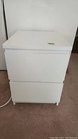 Front view of the white laminate two-drawer nightstand showing rectangular shape and drawer front details.