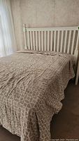 White wooden bed frame with vertical slat headboard and round finials, covered with beige comforter with a white circular pattern.