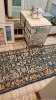 Photo of hooked runner rug on tiled floor next to rolling storage unit and reflecting mirror, shows part of lavender bath accessories on top of storage