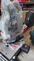 Band saw wrapped in plastic with visible motor and part of the frame.