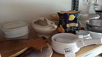 Image showing assortment of white ceramic dishes, a Biscotti ceramic jar with decorative hand-painted design, and wooden leaf-shaped trays on a shelf