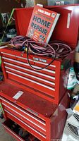 Shows two red metal Craftsman tool chests stacked with open top lid and miscellaneous cords and book inside.