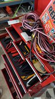 Red Craftsman tool chest with multiple drawers open, showing various hand tools such as pliers and cutters, with electrical cords coiled on top.