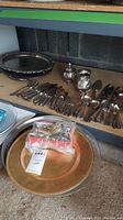 Photo showing large metal tray on floor, assorted flatware and serving pieces on shelf including sugar bowl and creamer