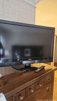 Full view of the Vizio 32 inch TV on a wooden dresser with remote control lying in front.