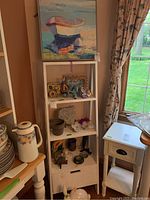 Wide view of white shelving unit with framed canvas art on top and various decorative items displayed on shelves including ceramic pieces and mineral specimens.